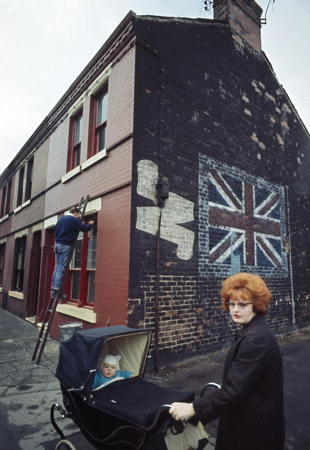 A mother takes her baby for a stroll past a Union Jack mural on a terraced street in Liverpool. By John Bulmer, 1965